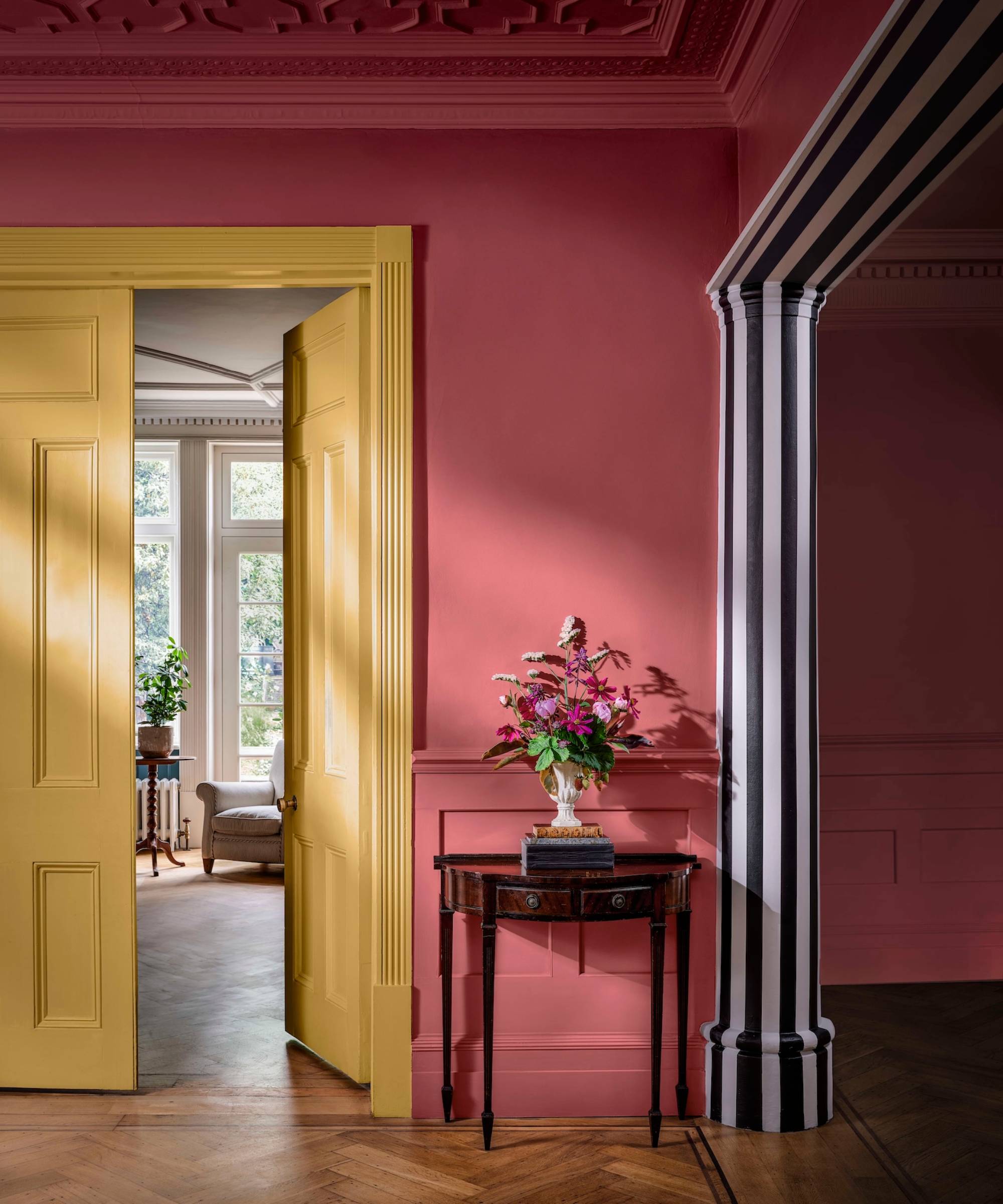 hallway with pink walls, yellow door and striped column and archway