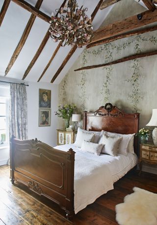 bedroom with beamed vaulted ceiling floral wallpaper dark wood bed and wooden floor with sheepskin rug