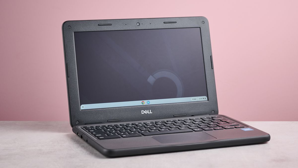 Three-quarter view of Dell Chromebook 3120 open on desk with pink wall in background