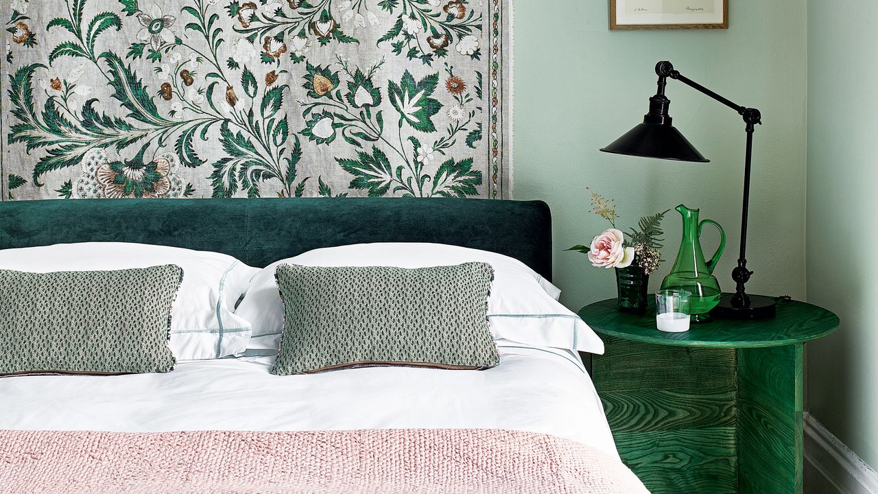 A green bedroom with a floral fabric wall hanging behind the bed