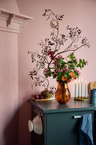 A floral arrangement of bouvardia in an orange glass vase on a dark wooden table in front of pale pink walls
