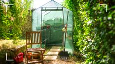 picture of greenhouse in domestic garden with chair and rake outside it