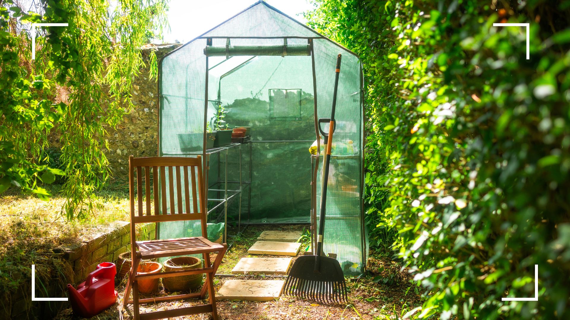 picture of greenhouse in domestic garden with chair and rake outside it
