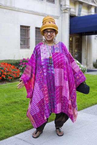 A photo of Marsha Music in an over 60 outfit featuring a pink caftan, black pants, and tan woven raffia hat.