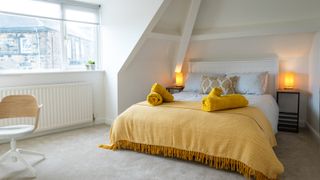 bedroom loft conversion with white walls and yellow blanket and towels on double bed