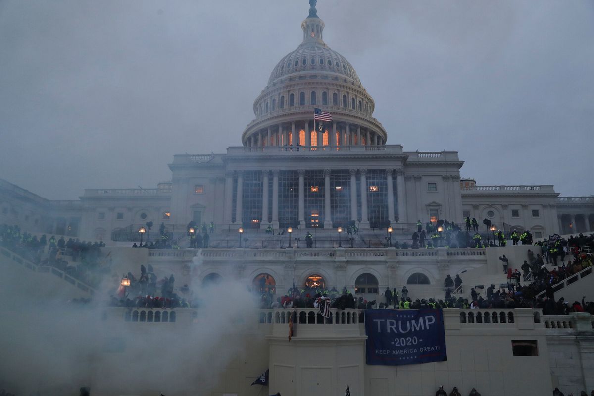 Capitol building with smoke surrounding it and rioters on it