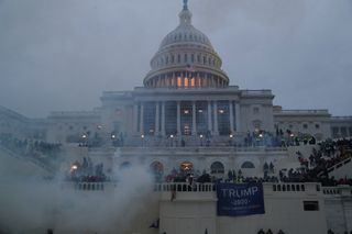 Capitol building with smoke surrounding it and rioters on it