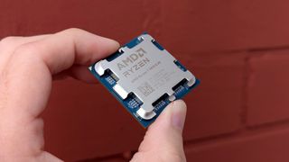 AMD Ryzen 7 9800X3D processor held in front of a red brick wall