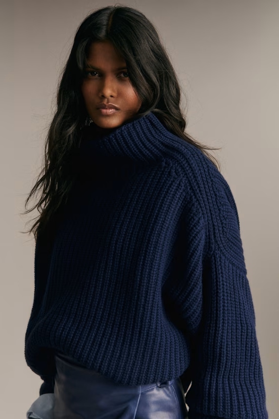 A model wearing a chunky blue turtleneck sweater.