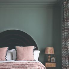 A bedroom with both walls and ceiling painted in a matt dark sage green paint with a curved headboard