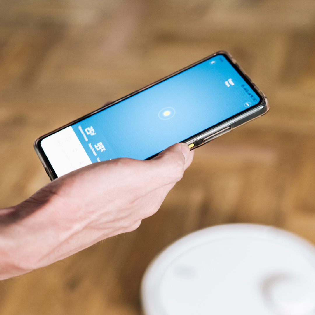 Hang holding smart phone over a white robot vacuum