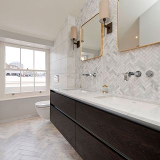 Classic white marble counter top with his and hers white wash basins with taps coming from the wall and 2 framed brass mirrors above it