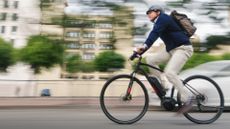 a professional businessman commutes to work on his electric battery powered ebike wearing casual business clothing and a helmet and backpack along a bike lane through the car traffic filled streets of San Diego, California, USA