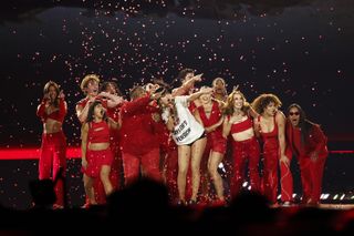 Taylor Swift onstage at the eras tour wearing an ashish shirt modeled after her 22 music video