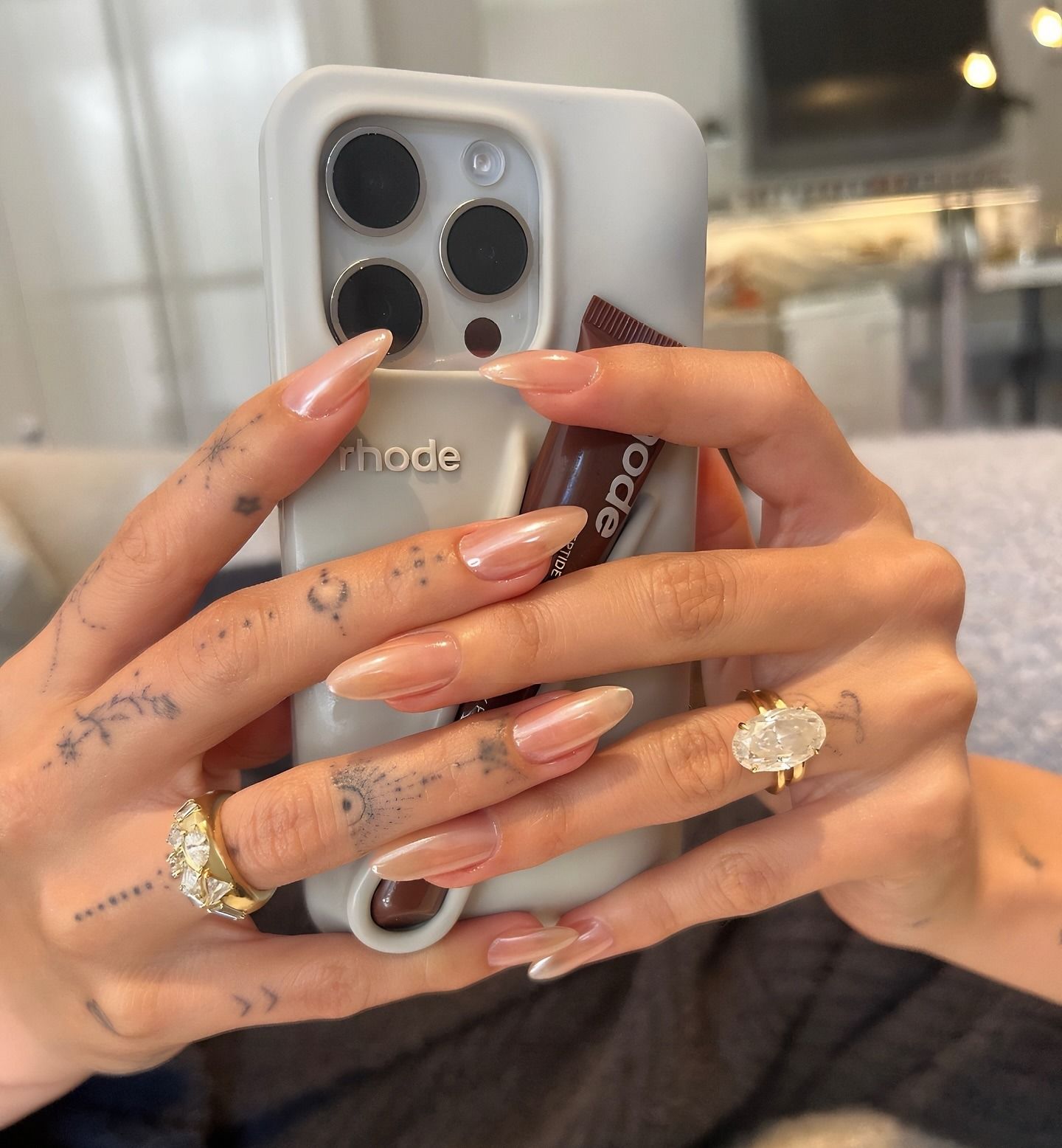 Hailey Bieber holding a Rhode phone case with a very light brown chrome manicure