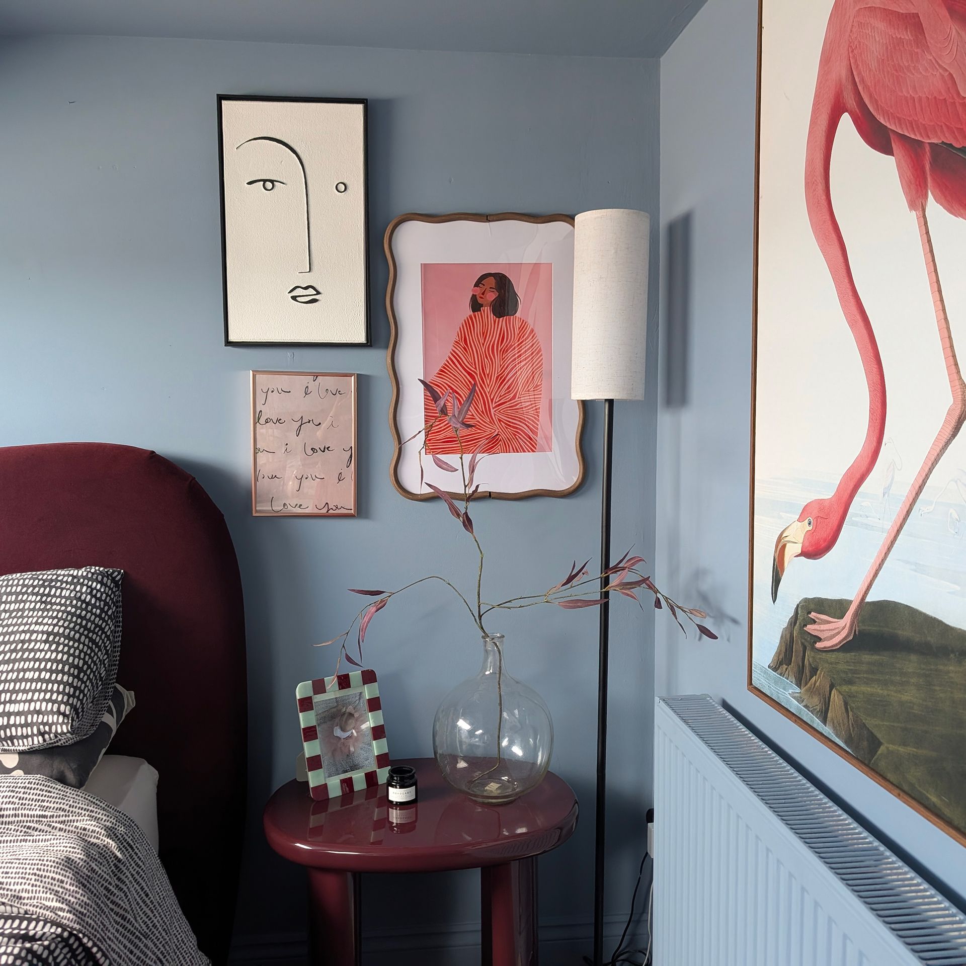 Blue bedroom with burgundy bed and bedside table, trio of framed prints on wall and large painting of flamingo above radiator