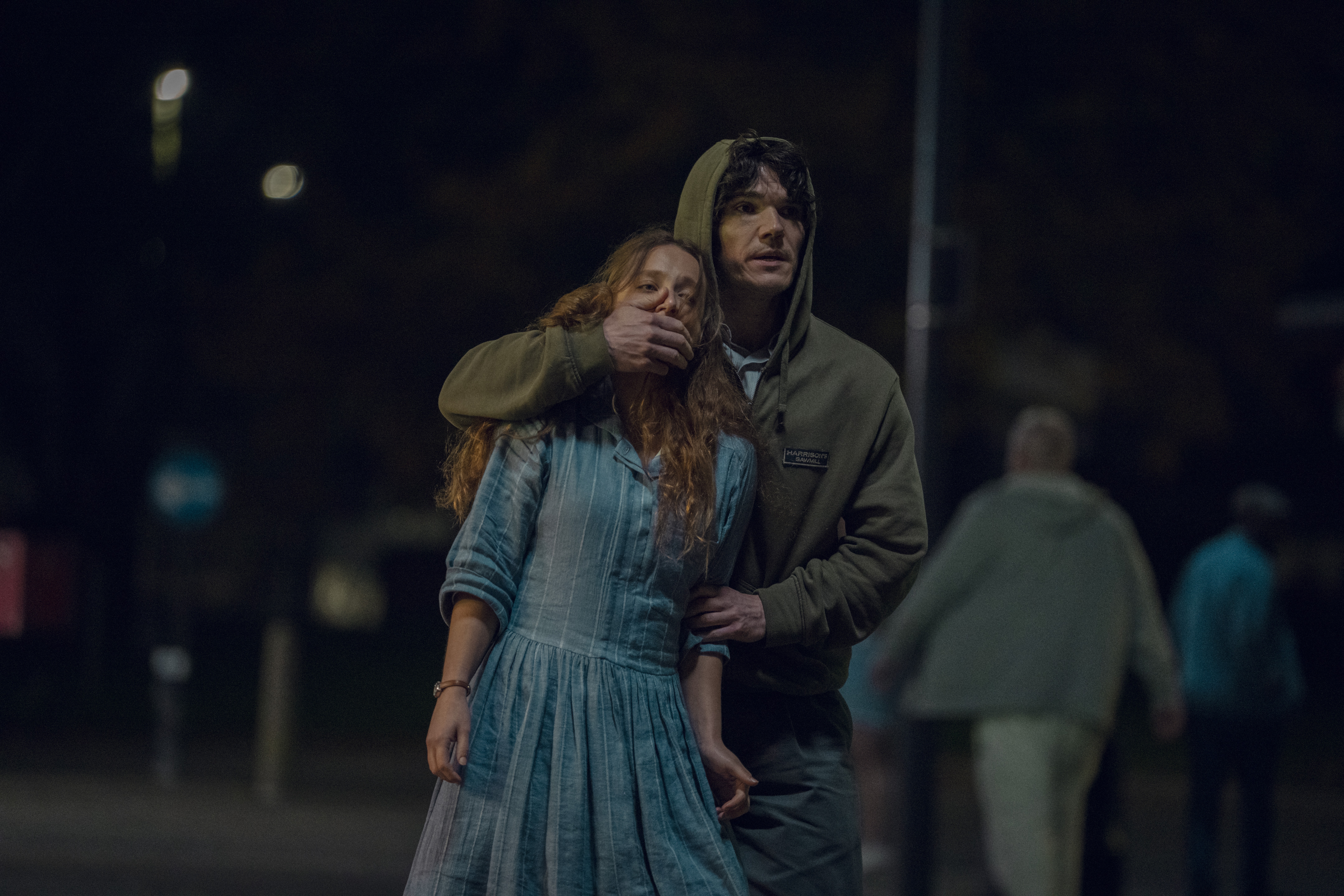 rosie's mouth is covered by sam as he walks her through a dark street in a still from netflix's unchosen