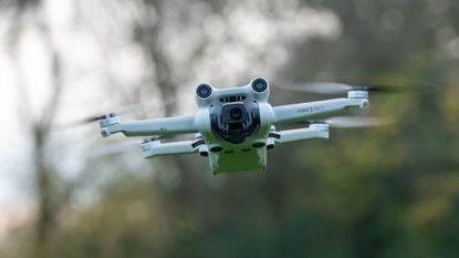 A DJI Mini 3 Pro drone is seen hovering above the ground. 