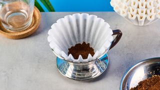 kalita wave stainless steel pour-over coffee dripper photographed against a blue background with kalita filters