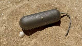 Beats Pill Bluetooth speaker on sandy beach next to seashell