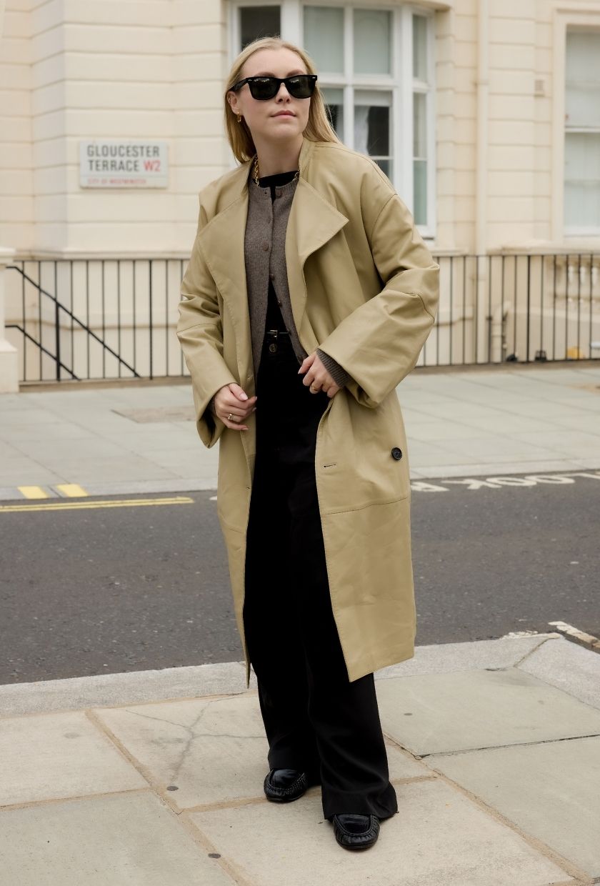 Woman wears beige trench coat, taupe cardigan and black trousers