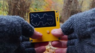 Two hands holding Playdate with woodland backdrop