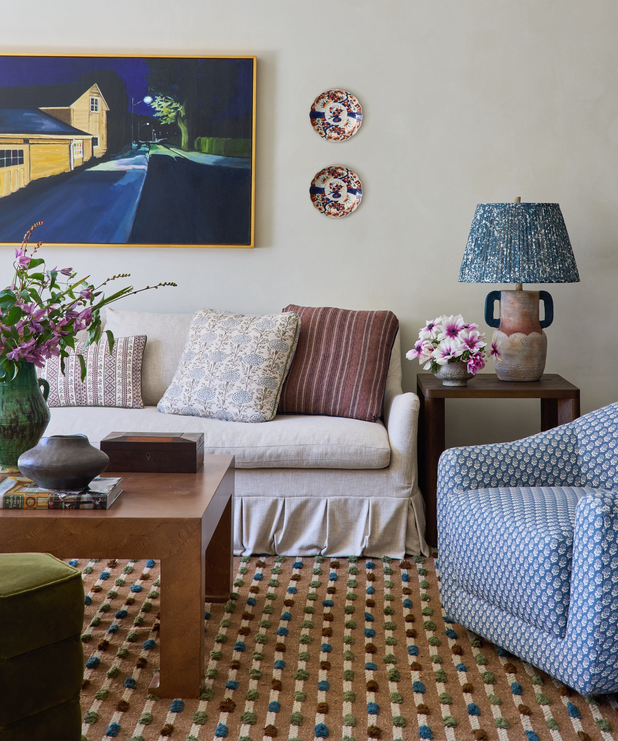 Living room with a linen skirted sofa, blue patterned armchair, Temple Studio rug, bespoke artwork and layered textiles.