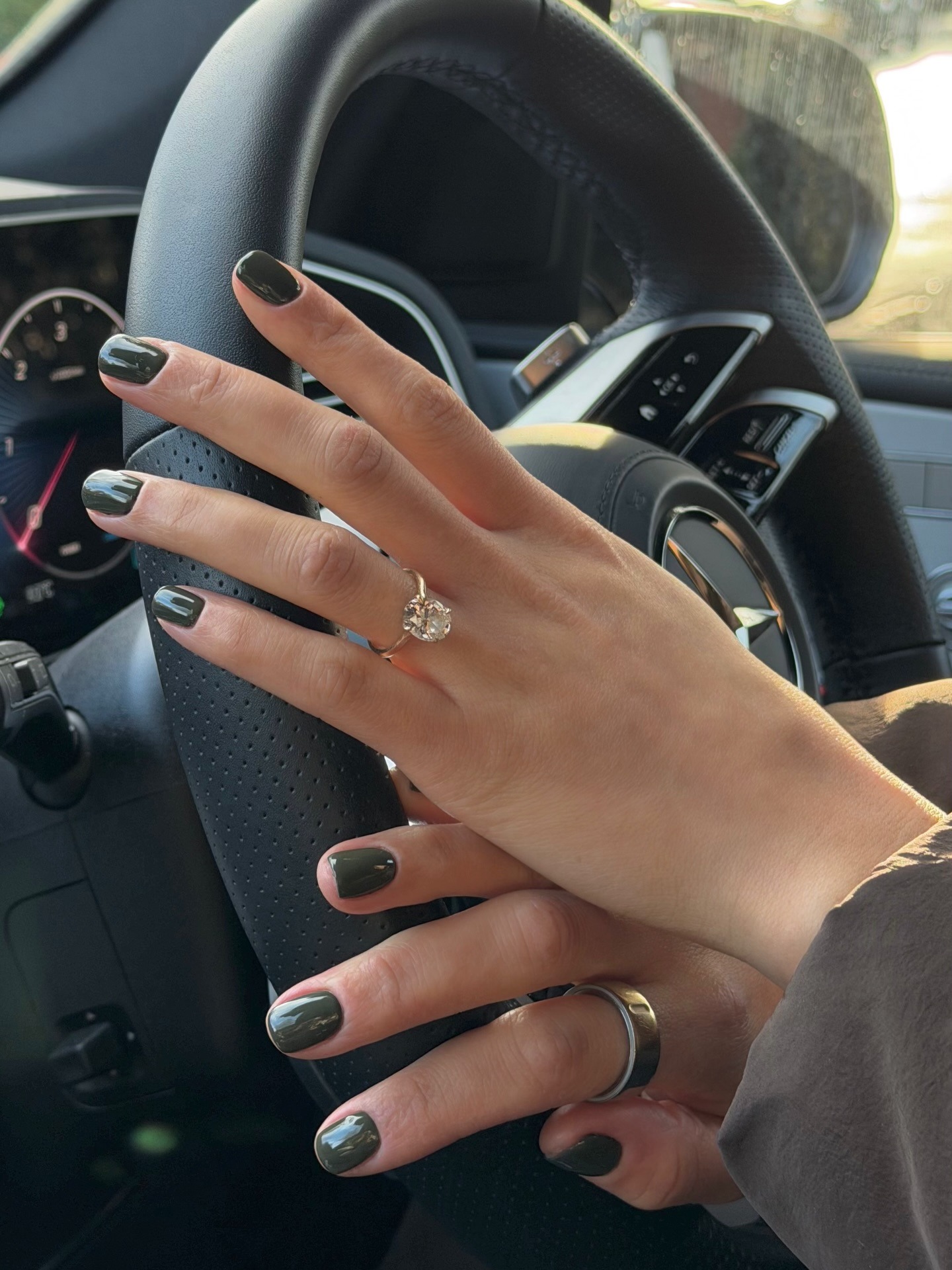 A woman's hands on a steering wheel with an earthy green manicure