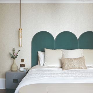 Bed with warm grey cushions and grey throw, navy headboard, warm grey wall and bedside table with plant