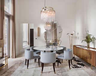 A grey dining room with marble dining table, large mirror and chandelier
