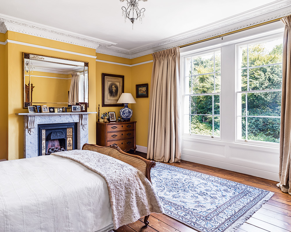 A bedroom with wooden floor, yellow walls and a large window