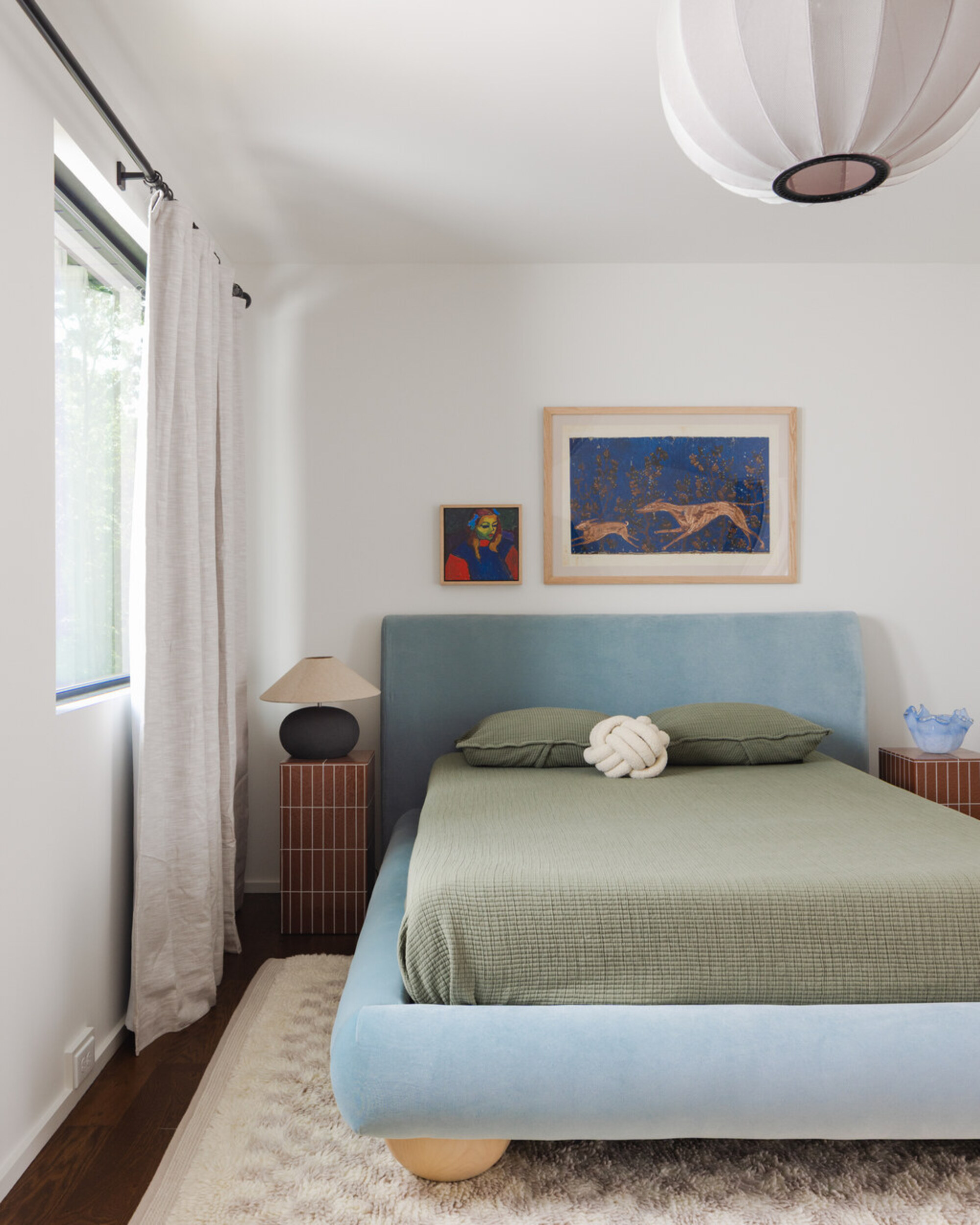a velvet blue bed frame and simple green bedding with a knot cushion and tiled bedside tables