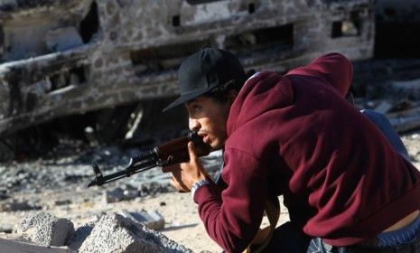 A rebel fighter ducks from incoming fire on a street in downtown Misrata, Libya: The EU may send up to 1,000 soldiers to ensure humanitarian aid reaches this rebel stronghold.