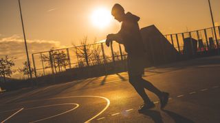Silhouette of a man walking and looking at a watch, on a basketball court at dawn