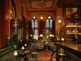 A warmly lit, classicism-inspired bar fuses art nouveau interiors including velvet, textural banquettes, sculptural table lights, floral motifs, and wooden surfaces with sophisticated contemporary lighting.