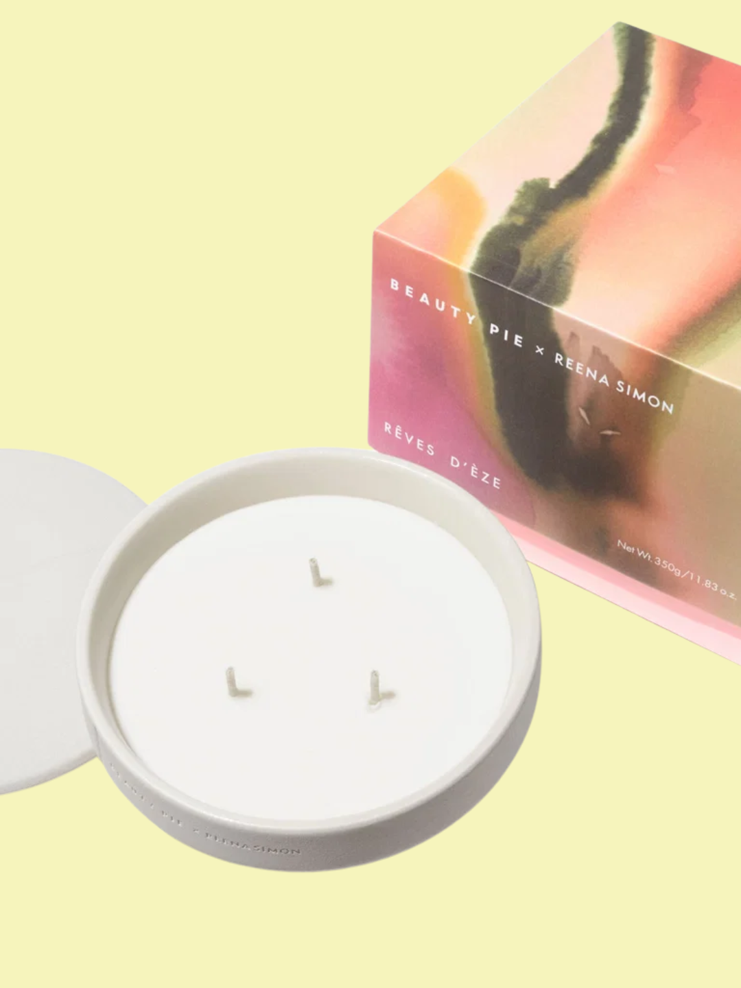 A ceramic three-wick candle with a lid from Reena Simon x Beauty Pie beside its colorful packaging