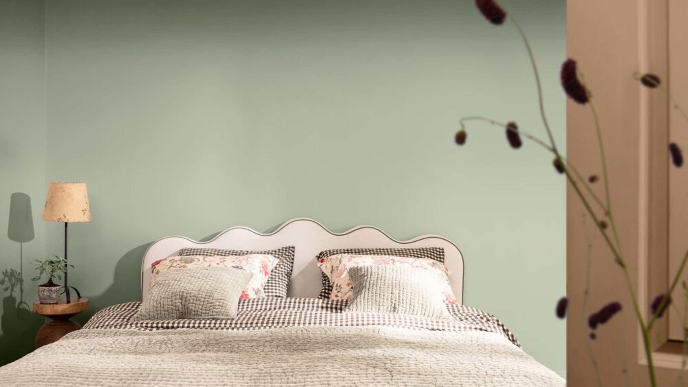 A bedroom painted in Dulux's Soulful Sage shade with a bed with a wavy headboard