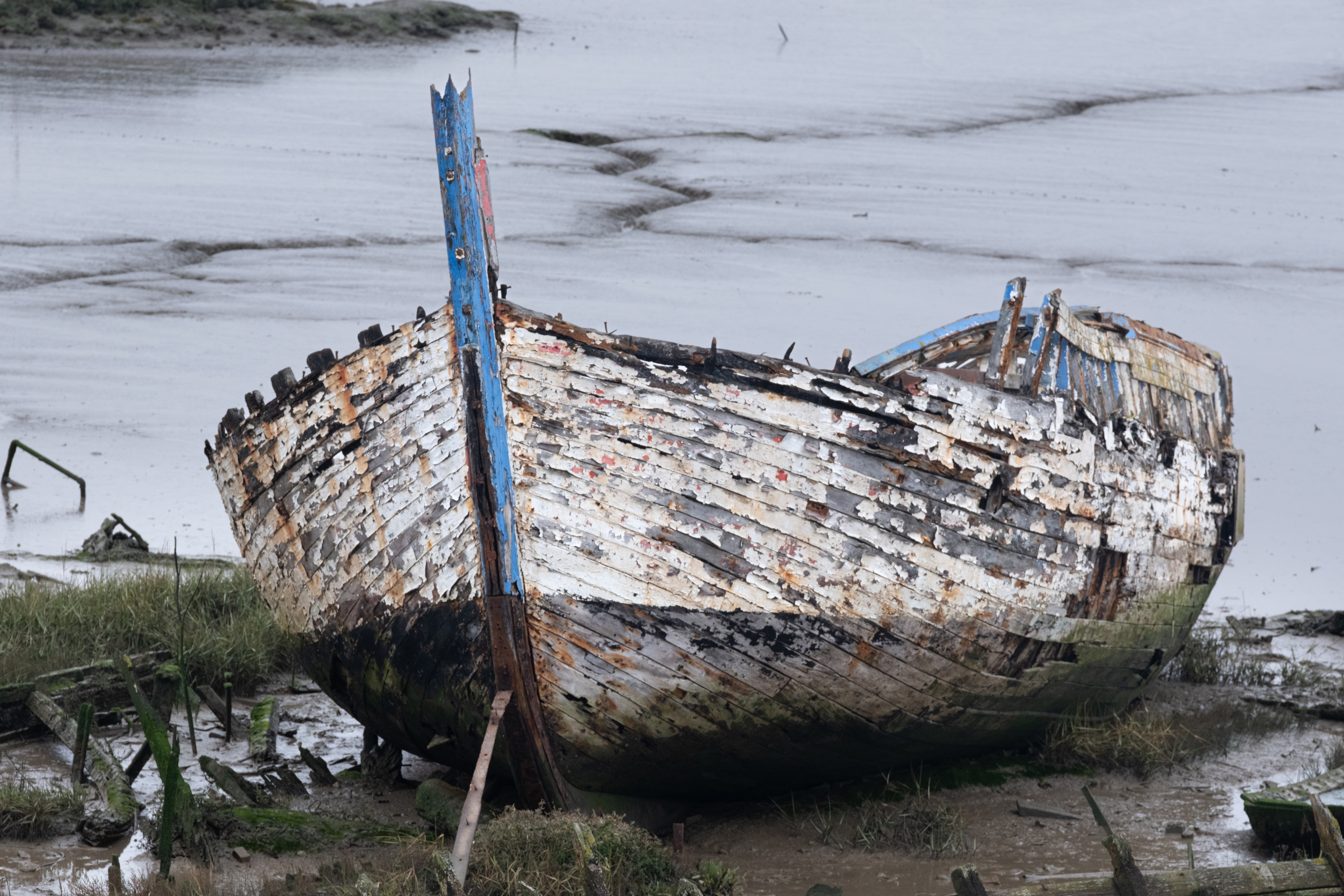 A shipwreck resting on the grass in front of mud flats