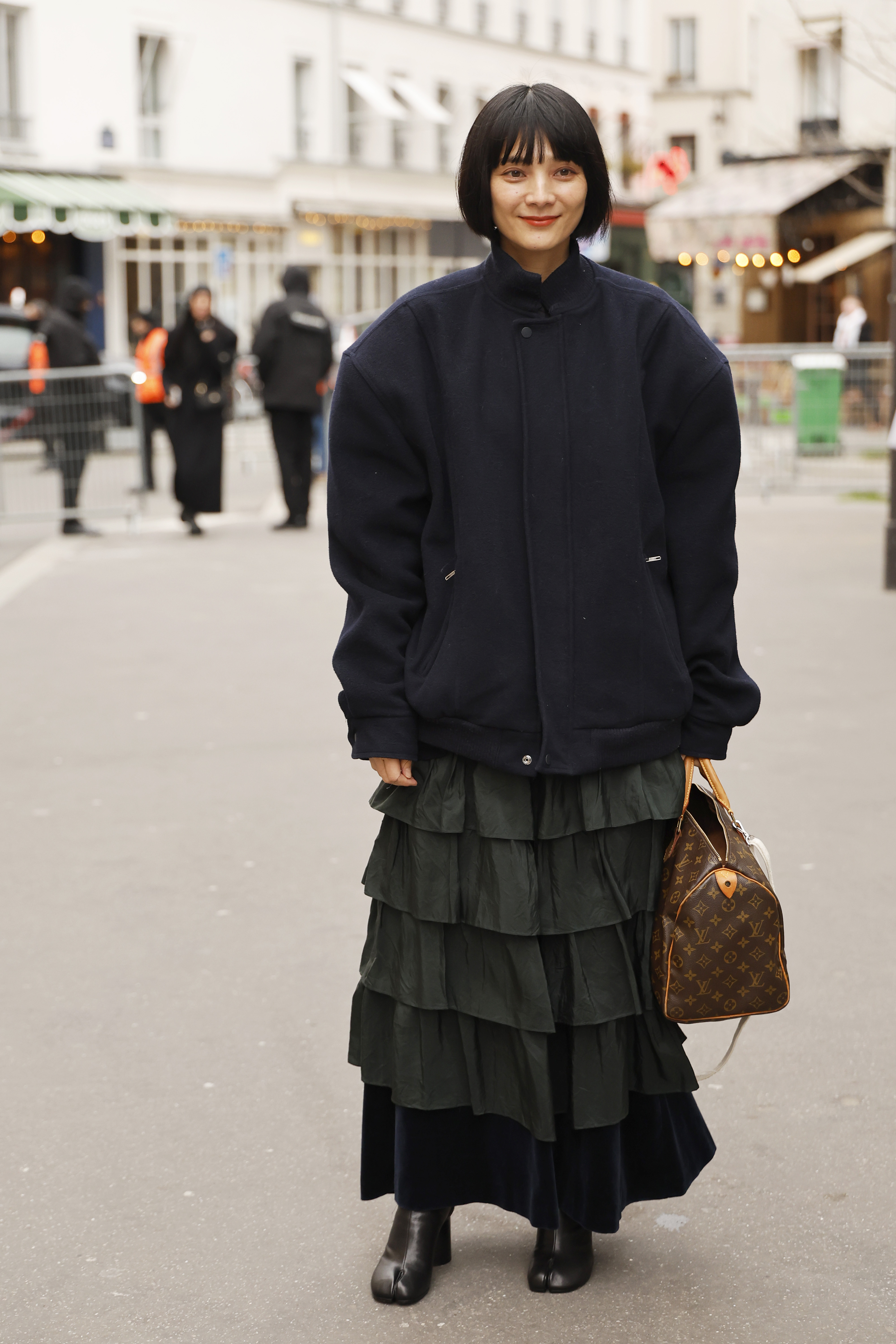 Aki Yoneda wears navy jacket, brown logo printed Louis Vuitton bag, olive green ruffled maxi skirt, black Maison Margiela tabi boots, outside Sacai, during the Menswear Fall/Winter 2026-2027 as part of Paris Fashion Week
