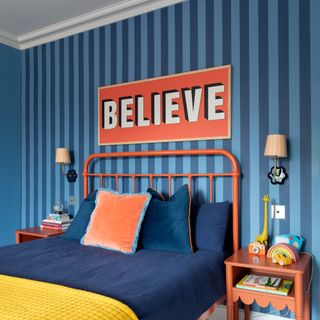 A bedroom with a blue striped wallpaper and a two striped wall lights above each bedside table