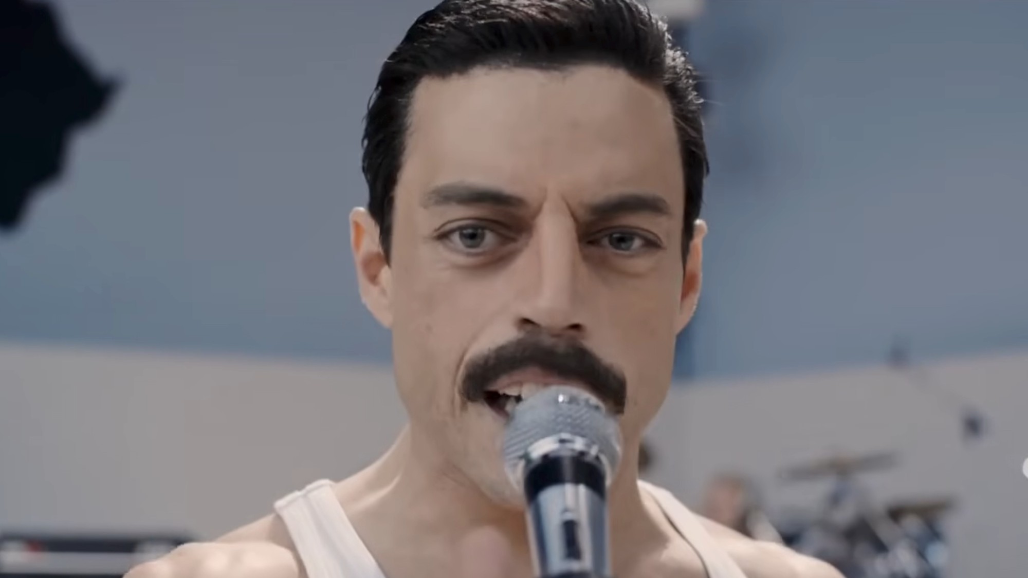 Rami Malek as Freddie Mercury with a mustache, singing into a microphone in Bohemian Rhapsody