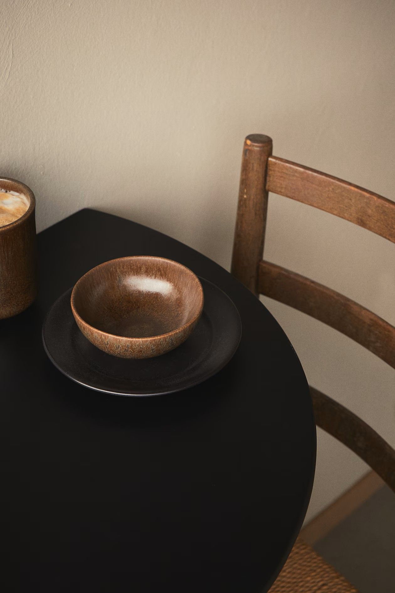 Close-up image of a black wall-mounted dining table. There is a plate, bowl, and coffee mug on the table, and a dining chair in view.