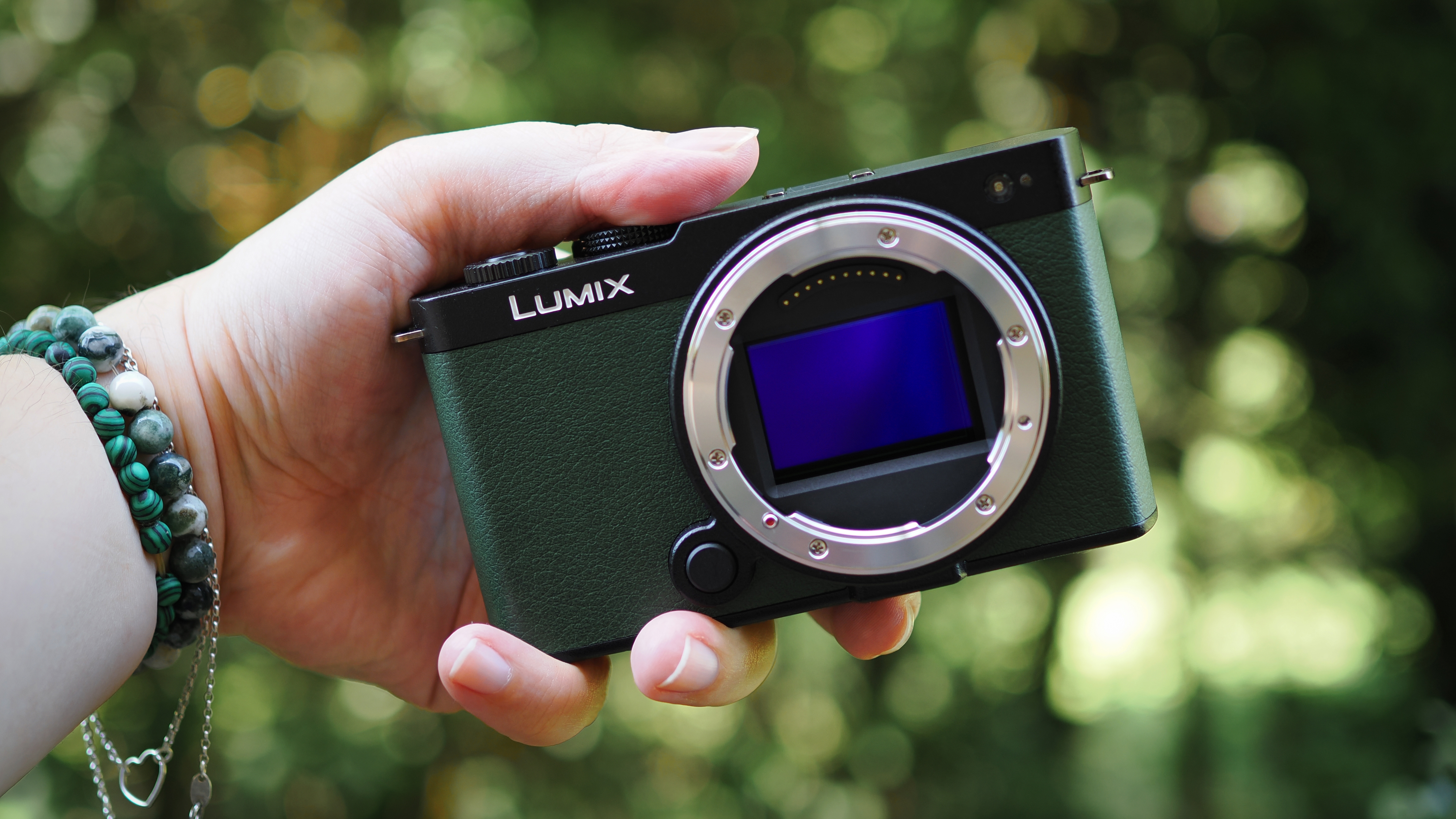 A Panasonic Lumix S9 with its sensor exposed, being held up outdoors in a rural setting