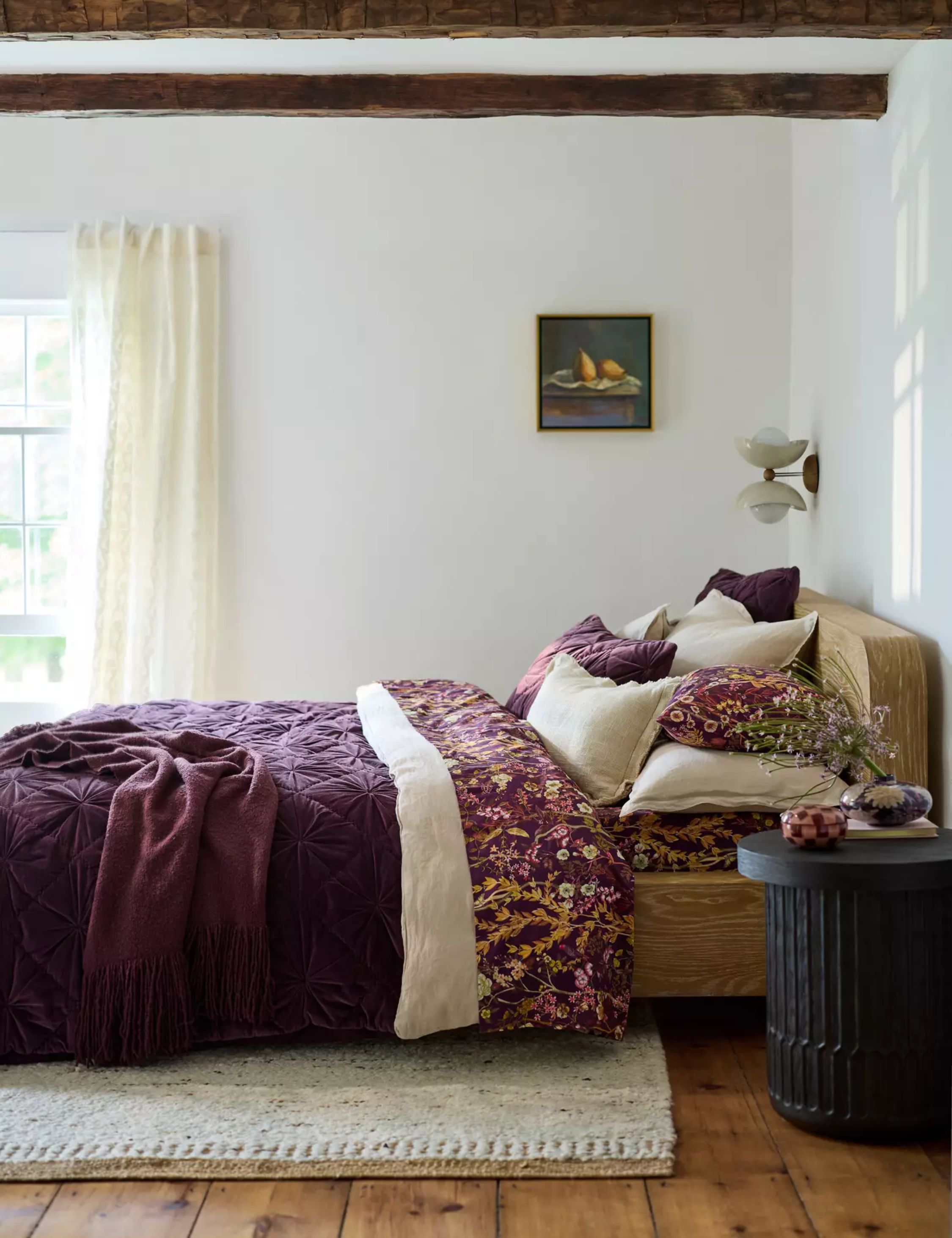 Characterful bedding with wide-plank wood floors, wooden ceiling beams, and burgundy bedding