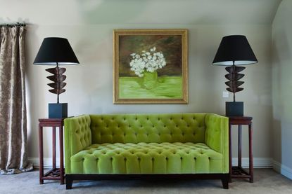 A green sofa flanked by wooden side tables with tall black table lamps