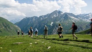 A group of hikers trek across a green mountainside on a partly cloudy day above Chamonix, France