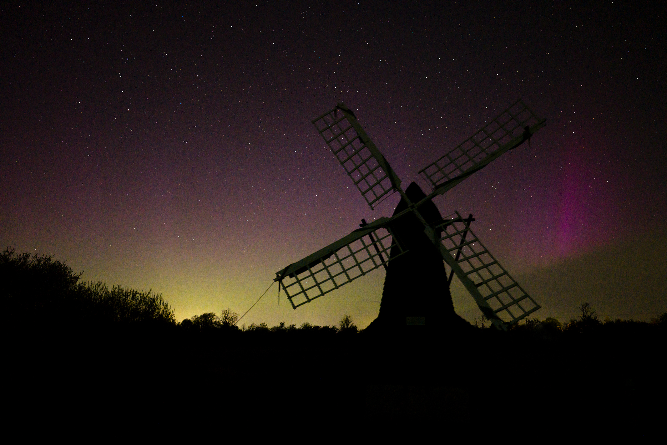 Aerial photograph of a windmill silhouette at night with the northern lights in the starry sky