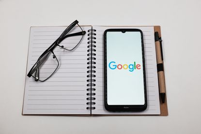  Google logo is displayed on a smartphone screen above a notebook next to glasses 