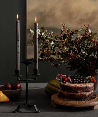 Halloween table decorated with black candles, a crow candle holder, and fruit and florals in gothic colors