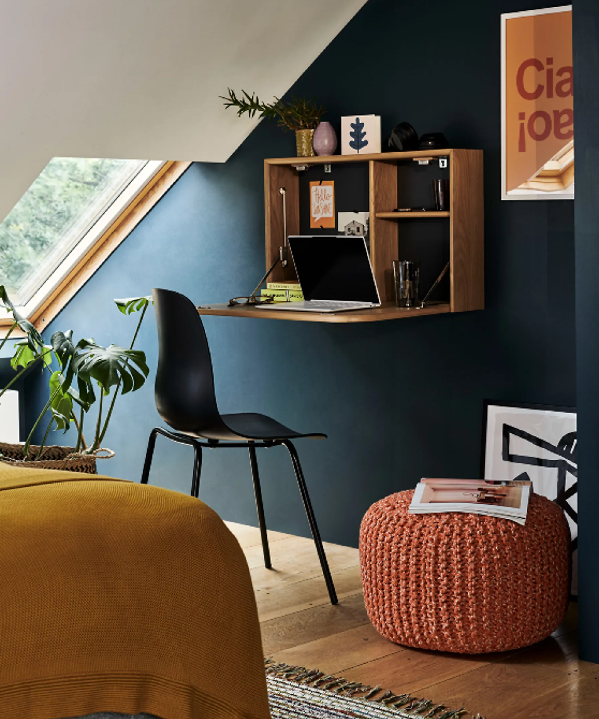 A flip-down wooden compact desk in a bedroom with a knitted coral footstool